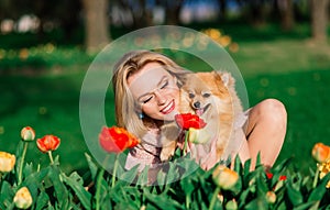 Attractive young woman holding dog spitz outside and smiling at camera, walking in the park