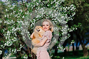 Attractive young woman holding dog spitz outside and smiling at camera, walking in the park