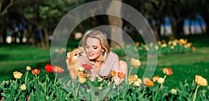 Attractive young woman holding dog spitz outside and smiling at camera, walking in the park