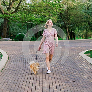 Attractive young woman holding dog spitz outside and smiling at camera, walking in the park