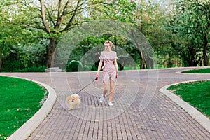 Attractive young woman holding dog spitz outside and smiling at camera, walking in the park