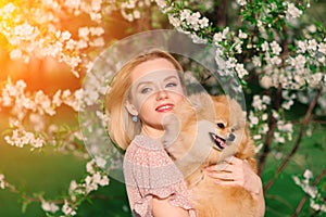 Attractive young woman holding dog spitz outside and smiling at camera, walking in the park.