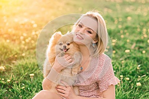 Attractive young woman holding dog spitz outside and smiling at camera, walking in the park.
