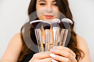 Attractive young woman holding golden makeup brushes. Professional makeup artist concept