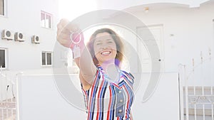 Attractive young woman holding keys while standing outdoor against new house.