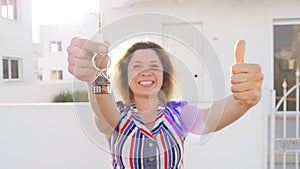 Attractive young woman holding keys while standing outdoor against new house.