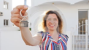 Attractive young woman holding keys while standing outdoor against new house.