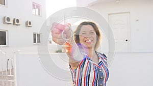 Attractive young woman holding keys while standing outdoor against new house.