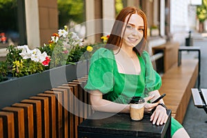 Attractive young woman holding mobile phone sitting at table with coffee cup in outdoor cafe terrace in sunny summer day