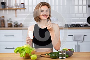 Attractive young woman holding vitamin capsule and glass of water at the kitchen. Beauty supplement.