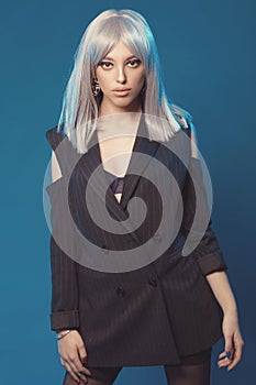 Attractive young woman in jacket and stockings on black shoes alluring posing. Fashion shoot in studio. Sexy poster with pretty