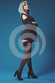 Attractive young woman in jacket and stockings on black shoes alluring posing. Fashion shoot in studio. Sexy poster with pretty