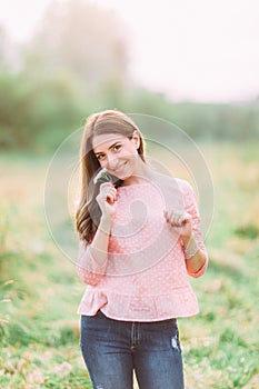 Attractive young woman in jeans and pink blouse enjoying her time outside in park with sunset in background.