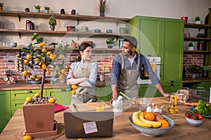 Attractive young woman in the kitchen together with her partner Afro American man looking something on the laptop then