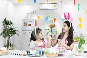 Attractive young woman with little cute girl are preparing for Easter celebration. Mom and daughter wearing bunny ears are