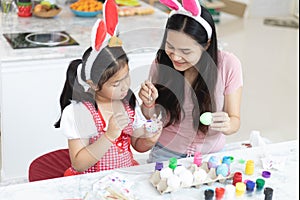 Attractive young woman with little cute girl are preparing for Easter celebration. Mom and daughter wearing bunny ears are