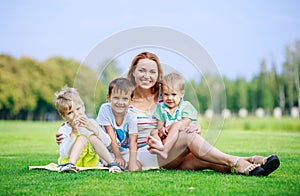 Attractive young woman with little sons sitting on grass in park