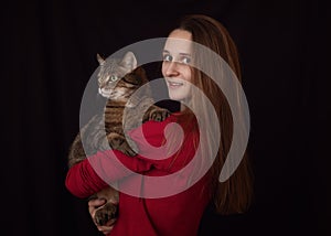 Attractive young woman with long hair with huge brown marble tabby male cat with green-yellow eyes in her arms