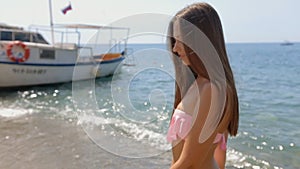 Attractive young woman with long straight hair in a pink bikini walking along the shore of the beach