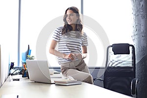 Attractive young woman looking away while sitting on the desk in office