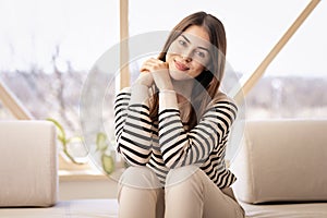 Attractive young woman looking at camera and smiling while relaxing on the sofa at home