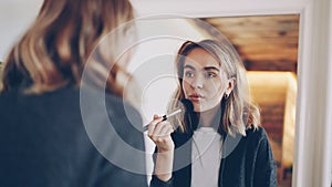 Attractive young woman is looking in the mirror and putting on make-up with brush and decorative cosmetics. Face