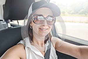 Attractive young woman making selfie on her smartphone. Female in the car making a photo shot on her phone