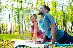 An attractive young woman and man doing yoga in green forest