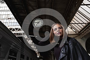 Attractive young woman millenial in black clothes and a hat and glasses at the railway station next to the train