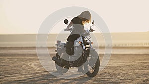 Attractive young woman motorcyclist makes a burnout on a motorcycle and ride away. Sunset or sunrise shot at desert. Female biker