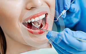 Attractive young woman with natural white teeth in dental clinic. Hands doctor dentist with medical tools. Healthy teeth concept