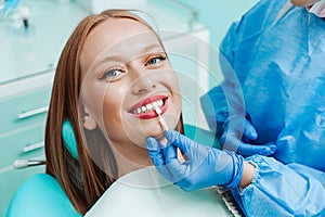 Attractive young woman with natural white teeth in dental clinic. Hands doctor dentist with teeth color palette next by face.