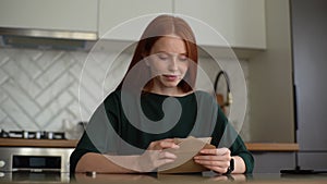 Attractive young woman opening envelope with letter, reading it and begins to feel happy at home.