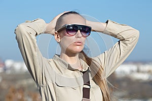 Attractive young woman in overalls similar to the uniform posing on open air with serious face and hands behind head