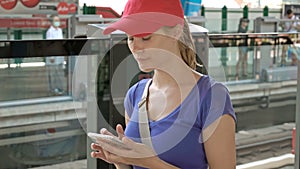 Attractive young woman on overground subway metro station checking her phone waiting train to arrive