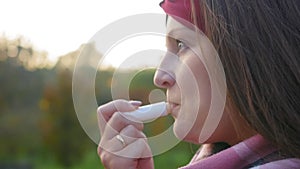 Attractive young woman paints her lips on a background of green forest. Girl paints her lips. Close up shot.