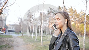 Attractive young woman in the park uses the phone. Walk through the city center in the evening. A young woman walks in a