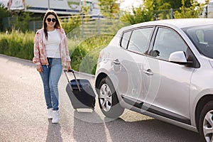 Attractive young woman parked the car and goes to airport with suitcase. Beautiful female traveling itself