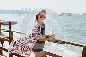 attractive young woman with plastic cup of cocktail on wooden pier in front