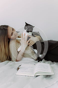 Attractive young woman playing with her cat and smiling while lying in bed at home. Cats friendly