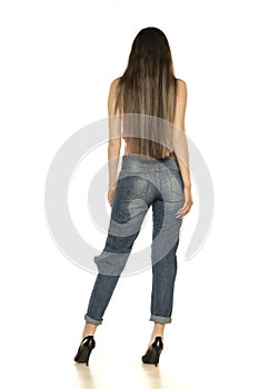 An attractive young woman posing in ripped jeans and summer shirt. Rear view on a white