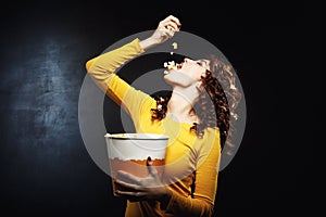 Attractive young woman pouring popcorn in mouth holding big bucket