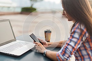 Attractive young woman reading a text message on her cell phone. Girl sitting outdoors using smartphone