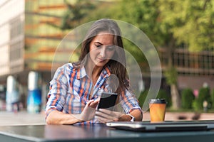 Attractive young woman reading a text message on her cell phone. Girl sitting outdoors using smartphone