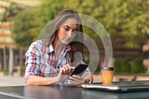 Attractive young woman reading a text message on her cell phone. Girl sitting outdoors using smartphone