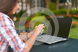 Attractive young woman reading a text message on her cell phone. Girl sitting outdoors using smartphone