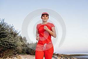 An attractive young woman in a red tracksuit stands on top of a mountain