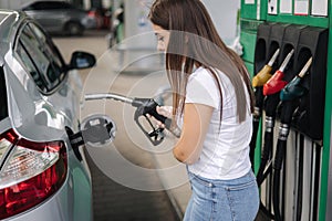 Attractive young woman refueling car at gas station. Female filling diesel at gasoline fuel in car using a fuel nozzle