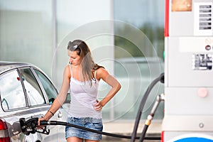 Attractive, young woman refueling her car in a gas station photo