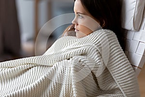 Attractive young woman relaxing under soft blanket in comfortable chair